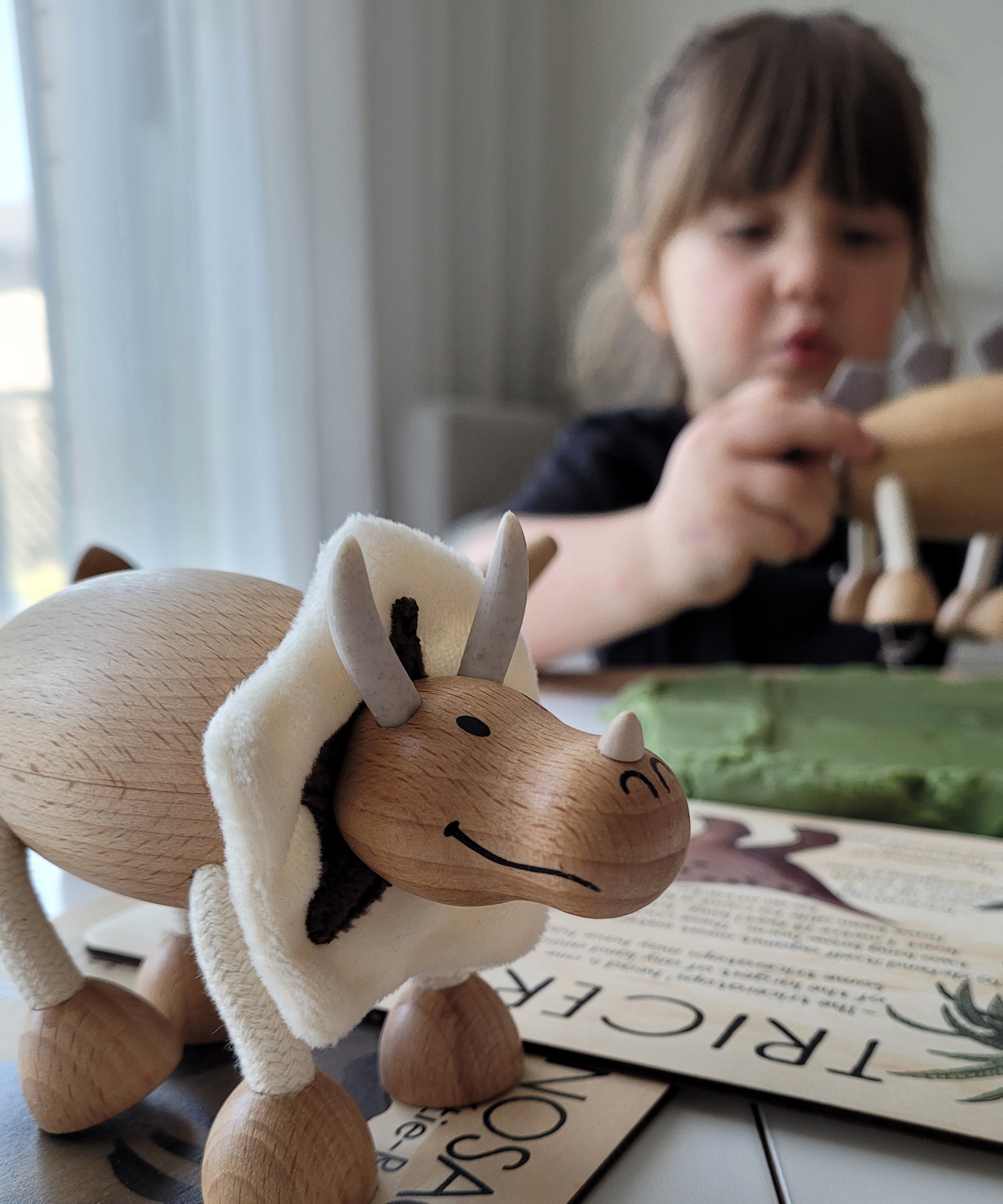 wooden dinosaur toy on a table with a small girl in the background playing another wooden dinosaur toy