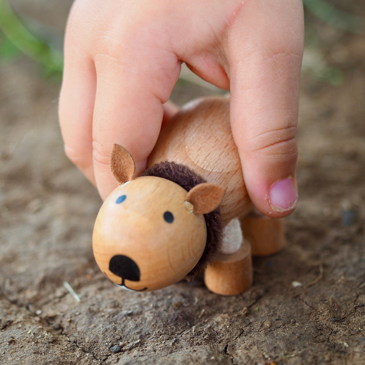 Small wooden wombat figurine held by a child's hand on dirt background