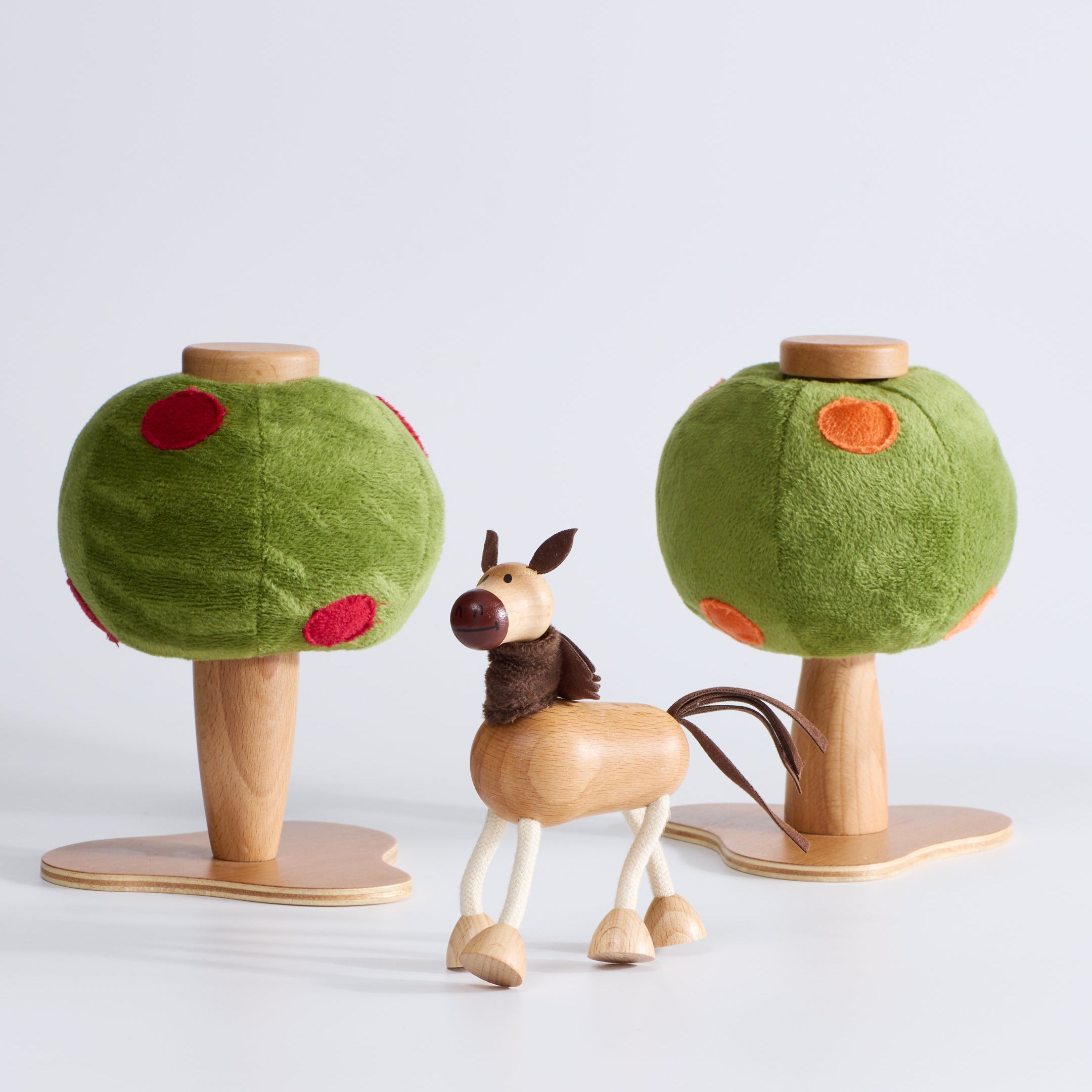 Anamalz Apple Tree toy with a green plush top and red spot apples, standing on a wooden base next to an Anamalz orange Tree toy with a green plush top and orange spots, standing on a wooden base with a wooden toy horse in the centre