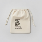 A beige fabric drawstring pouch with black printed text, including the brand name 'anomaliz' and a quote, laid flat on a wooden surface.