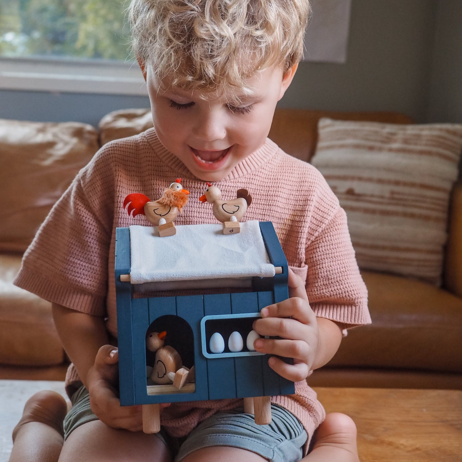 Child playing with a toy barn set in a living room.