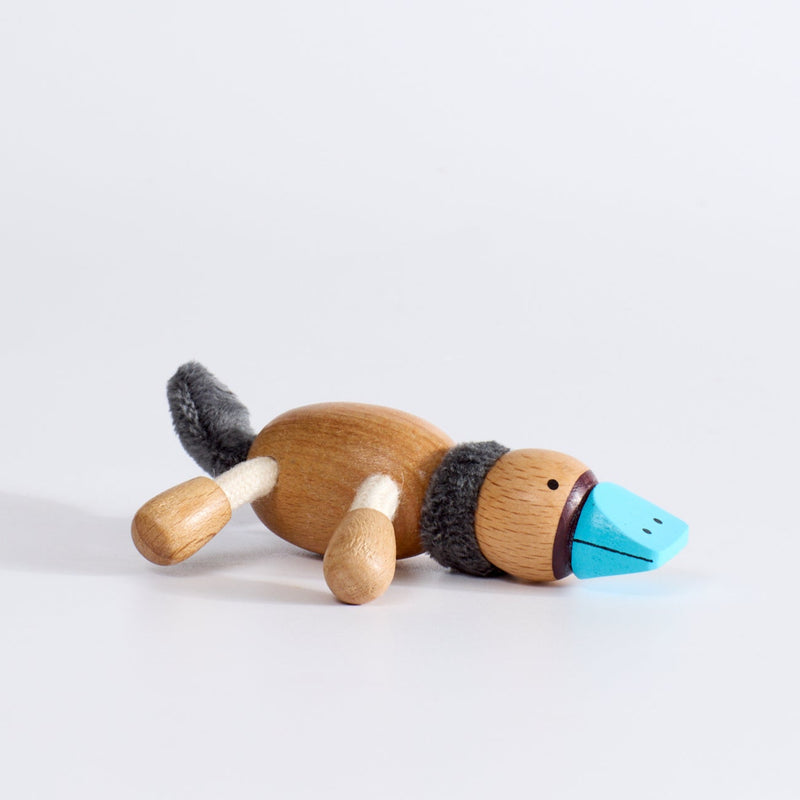 A plush toy platypus, with beige body, black tail, and blue accents on its face and feet.